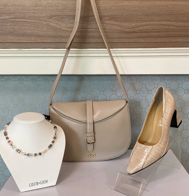 Beige leather shoulder bag displayed with matching quilted heels and beaded necklace on retail display