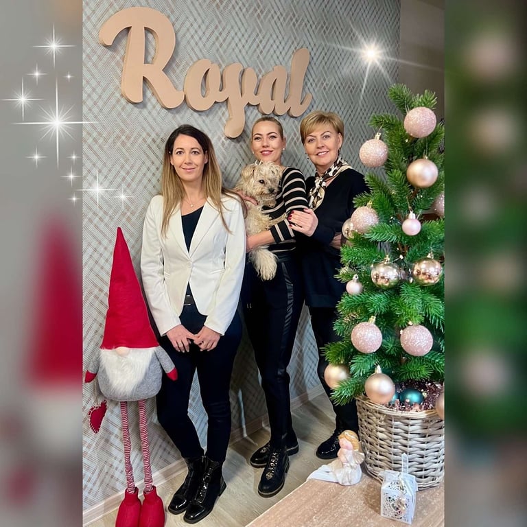 Three women posing in front of a festive Christmas display with gold Royal sign and decorated tree with white and gold ornaments