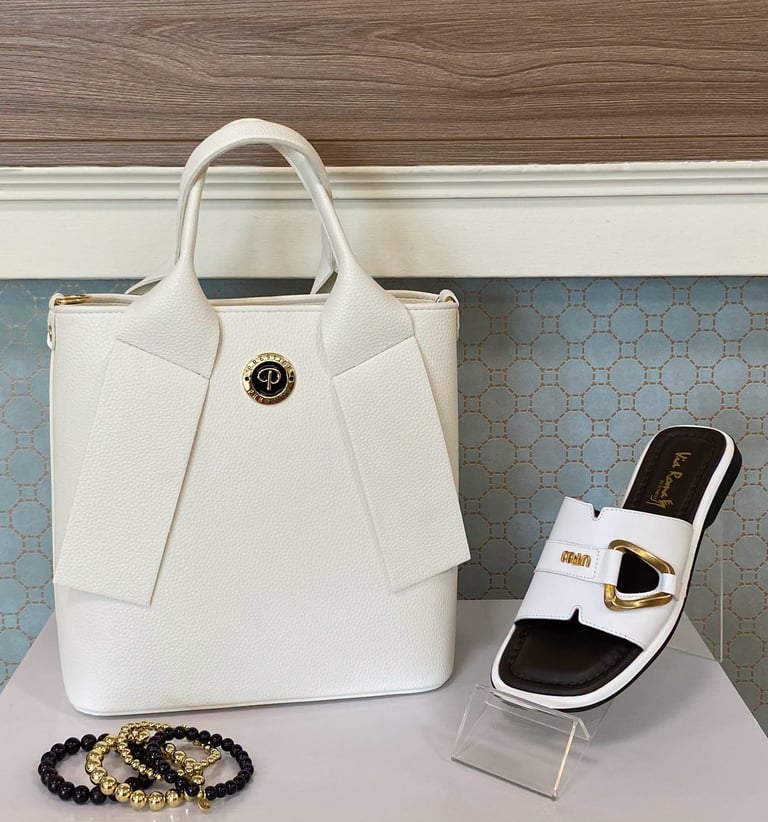 White designer handbag with white and black sandal and beaded bracelets displayed on a shelf