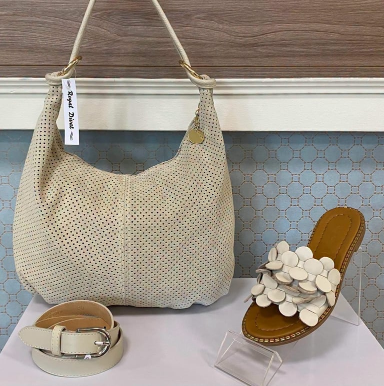 Beige woven hobo bag with matching belt and decorative wooden sandals displayed on white shelf against patterned wallpaper
