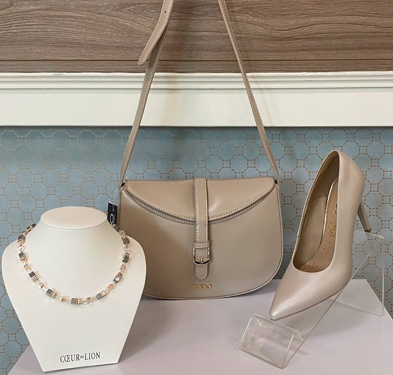 Beige leather handbag, champagne heels, and gold chain necklace displayed on a white bust and table