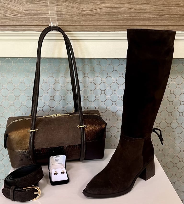 Brown leather handbag, black knee-high boot, earrings display, and black shoulder strap arranged on white shelf