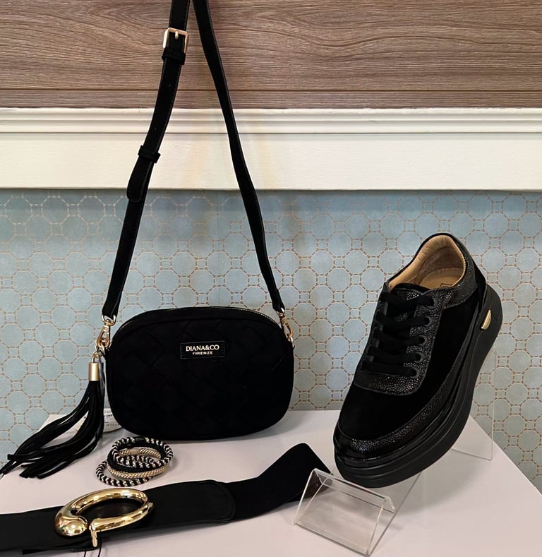 Black velvet crossbody bag with gold accents displayed alongside black lace-up shoe, gold bangles, and black hair clip