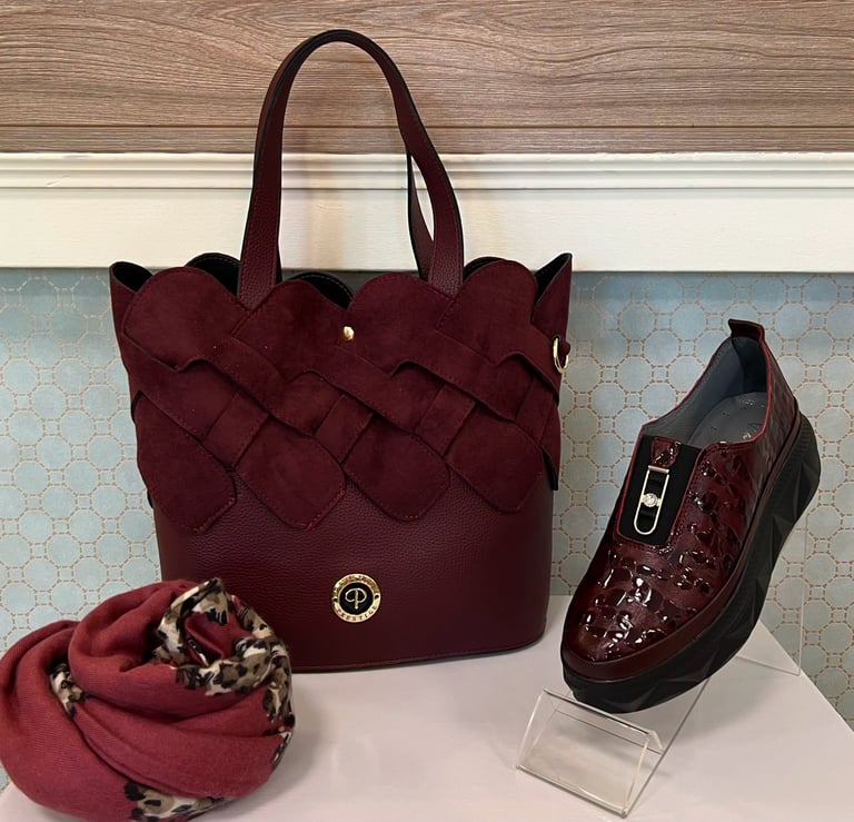 Burgundy quilted tote bag with matching patent leather loafer shoe and burgundy scarf displayed on white shelf