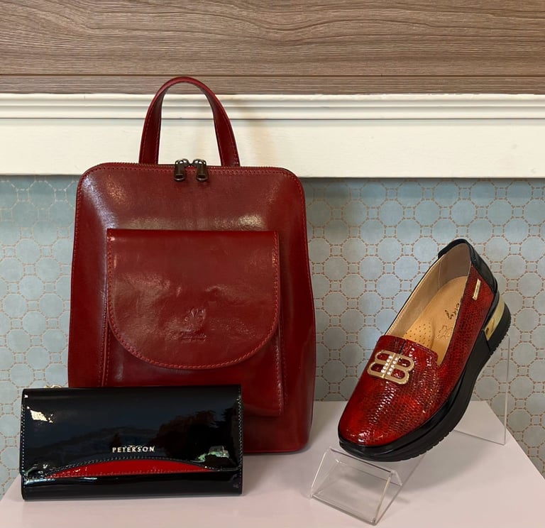 Red leather backpack, black patent wallet, and burgundy sequined loafer displayed on a shelf