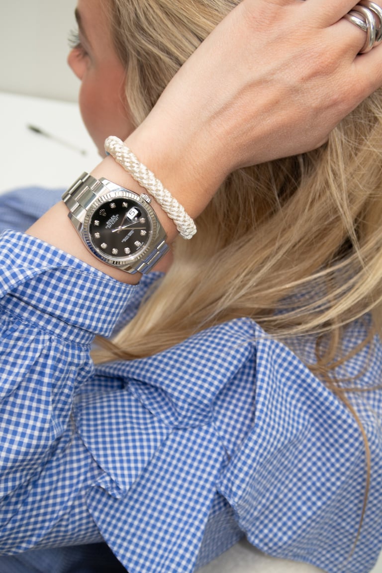 Woman wearing blue gingham shirt with black diamond watch and white beaded bracelet, hand in hair