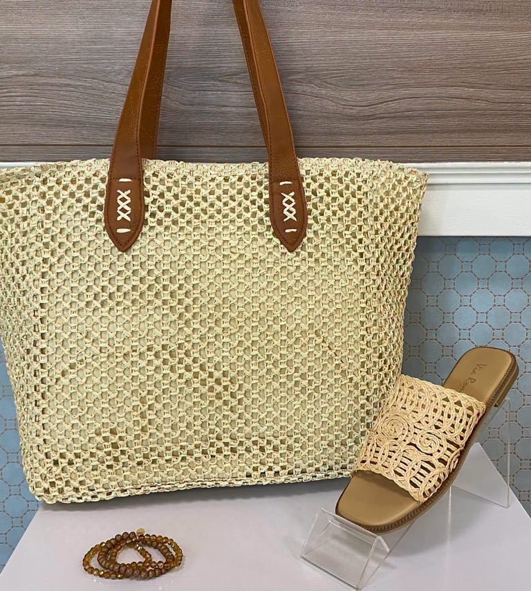Cream woven tote bag with brown leather handles displayed with matching sandals and beaded bracelet