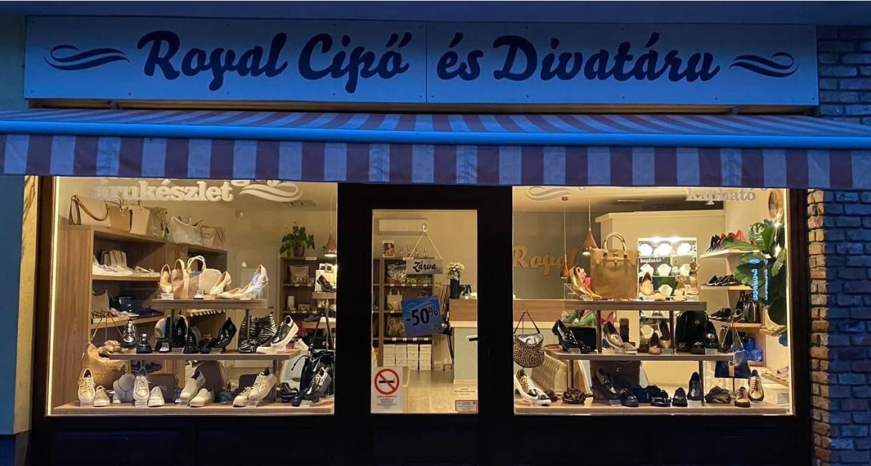 Storefront of Royal Cipő és Divatáru boutique at night with illuminated display windows showing merchandise