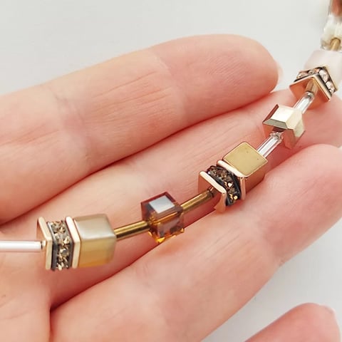Delicate gold and gemstone bracelet displayed on an open palm, showing multiple square crystal sections with metallic settings
