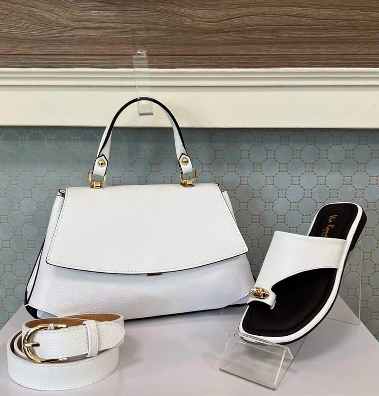 White leather handbag with gold hardware displayed alongside matching white belt and black and white slide sandal