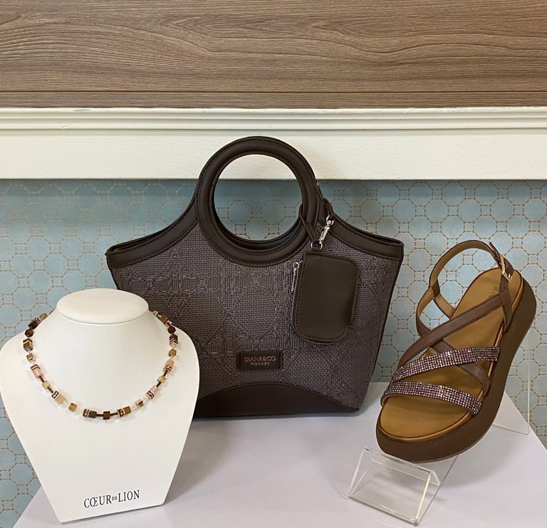 Display of accessories including brown quilted handbag, beaded necklace on stand, and brown strappy sandal