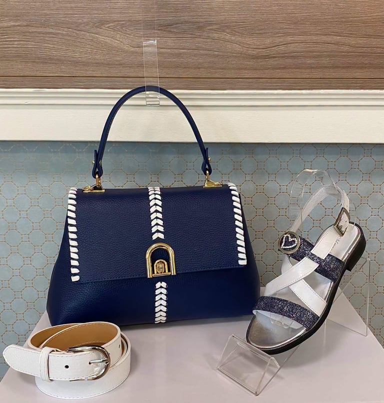 Navy blue leather handbag with white stitching, white belt, and black and white striped sandal displayed on pale surface