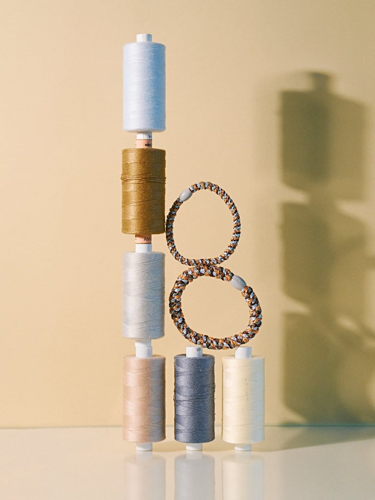 Stacked spools of colorful thread with beaded bracelets arranged vertically against a beige background