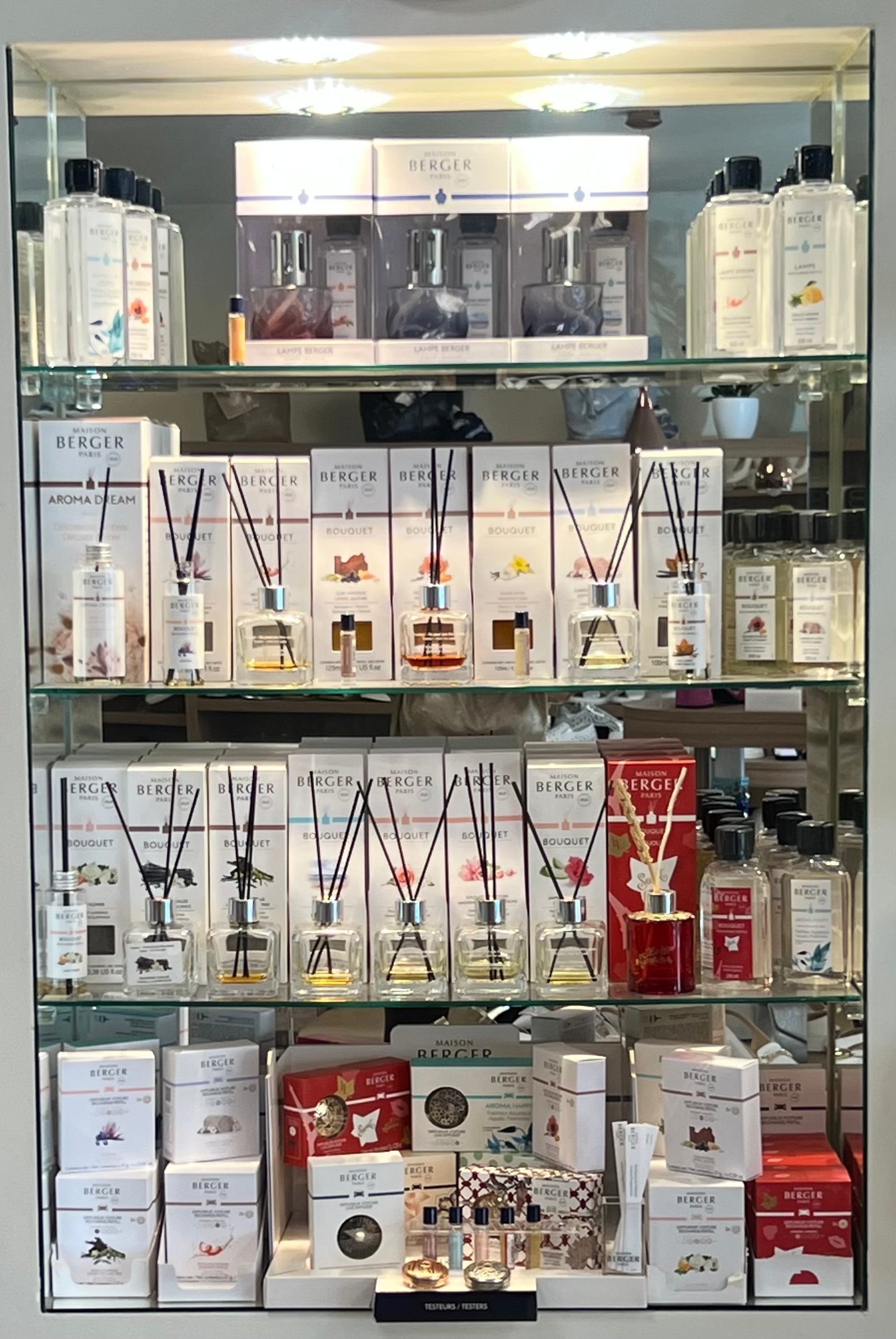 Glass display cabinet showing Berger home fragrance products including reed diffusers, room sprays, candles, and scent accessories arranged on four shelves