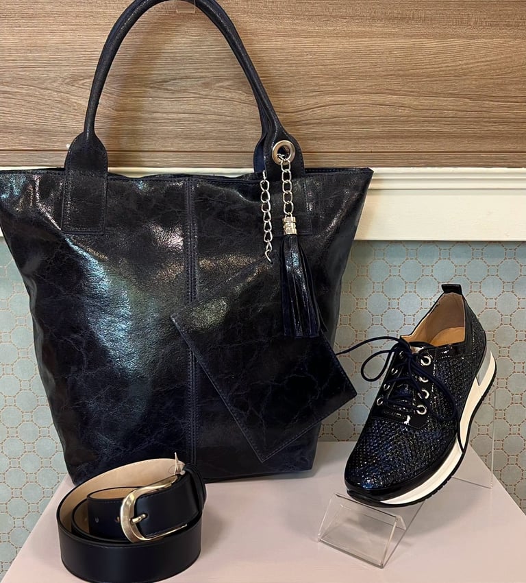 Black leather tote bag with matching belt and sparkly sneaker displayed on a wooden floor