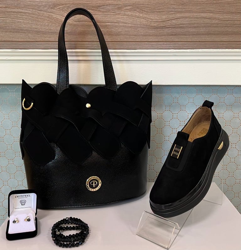 Black leather cat-eared tote bag with gold accents, displayed alongside black suede loafer, stud bracelet, and small jewelry box