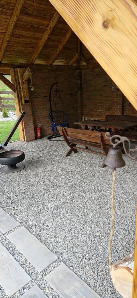 Interior of a brick garage or shed with wooden beam ceiling, gravel floor, hanging bicycle, furniture, and fire pit