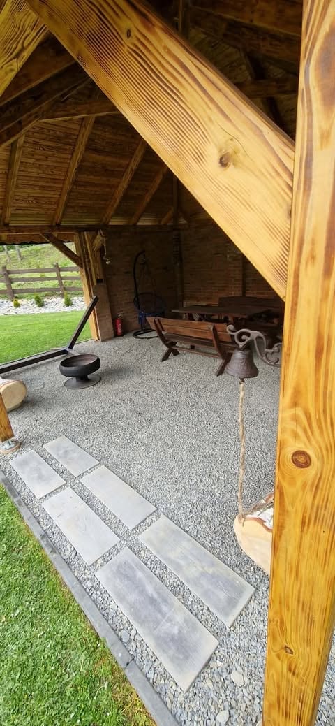 Interior of a wooden gazebo or pavilion with gravel flooring, stone stepping stones, and rustic furnishings visible