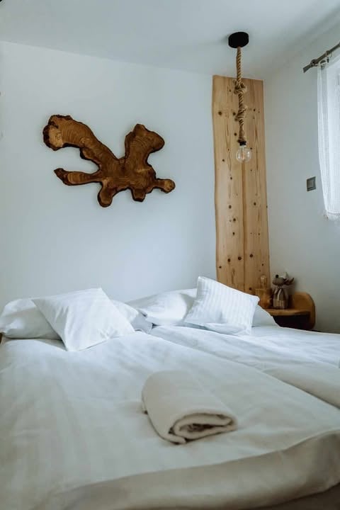 Minimalist bedroom with white bedding, wooden wall art above bed, and wooden pendant light fixture