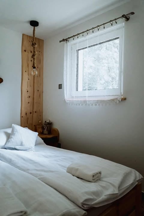 Minimalist bedroom with white bedding, wooden headboard with hanging crystals, and window with white lace curtains