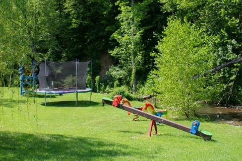 Children playing on a seesaw in a backyard with a trampoline and trees in the background