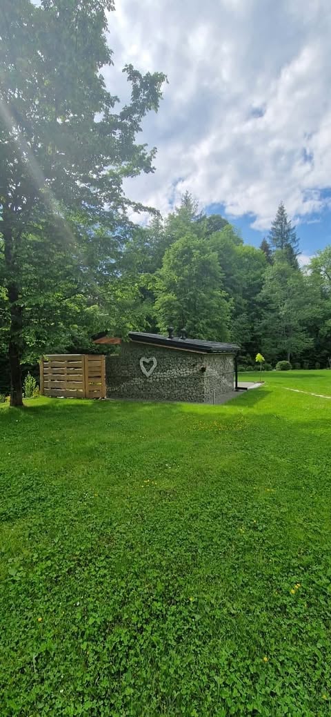Stone building with heart carved on it in grassy meadow surrounded by trees and blue sky