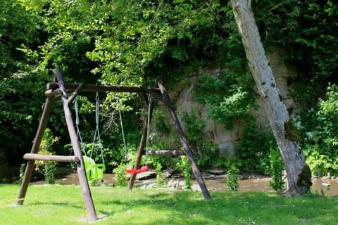 Wooden swing set in a green park with ivy-covered stone wall and large tree in background