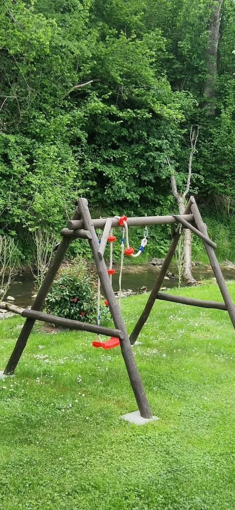 Wooden swing set with red seats in a grassy yard surrounded by dense green trees and vegetation