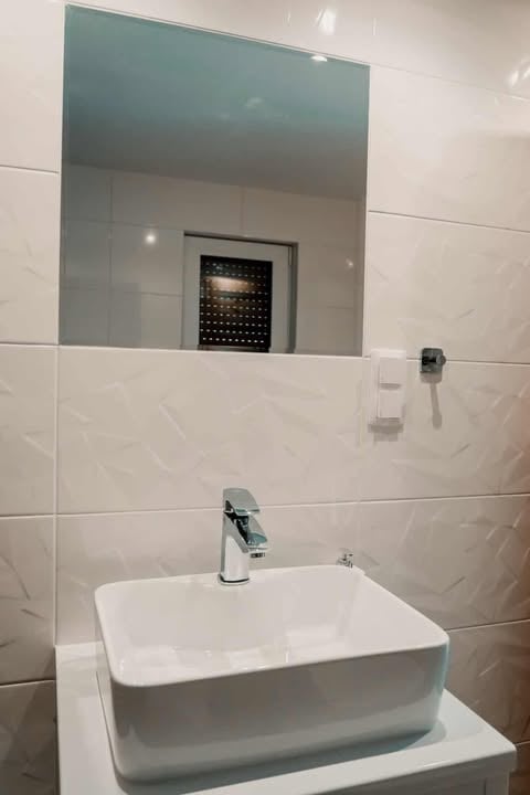 Modern bathroom vanity with white rectangular sink, chrome faucet, and large mirror reflecting tiled walls and recessed lighting