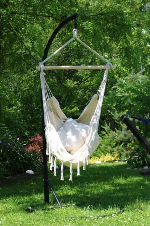 White macramé hanging chair suspended from black metal frame in lush green garden setting