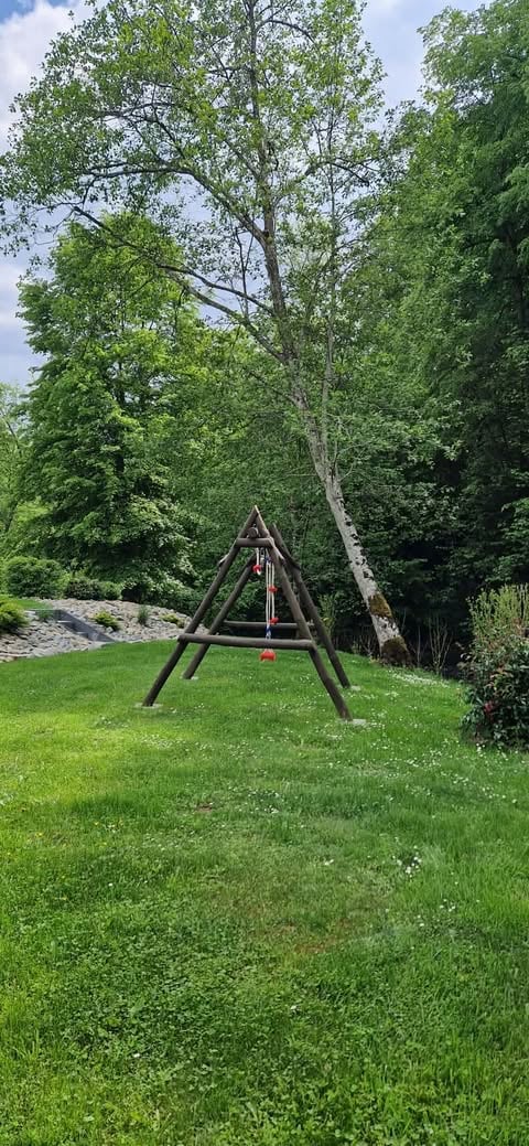 A-frame wooden swing set in a grassy park surrounded by tall green trees on a sunny day