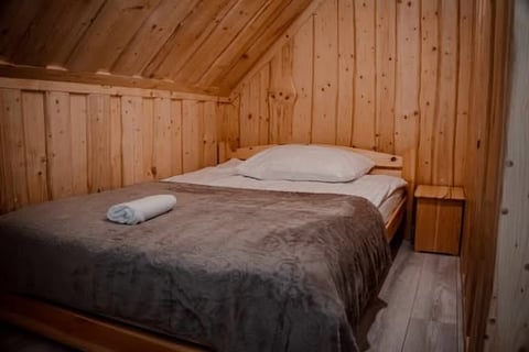 Cozy wooden cabin bedroom with a bed covered in dark bedding, white pillows, and a small wooden nightstand against paneled walls