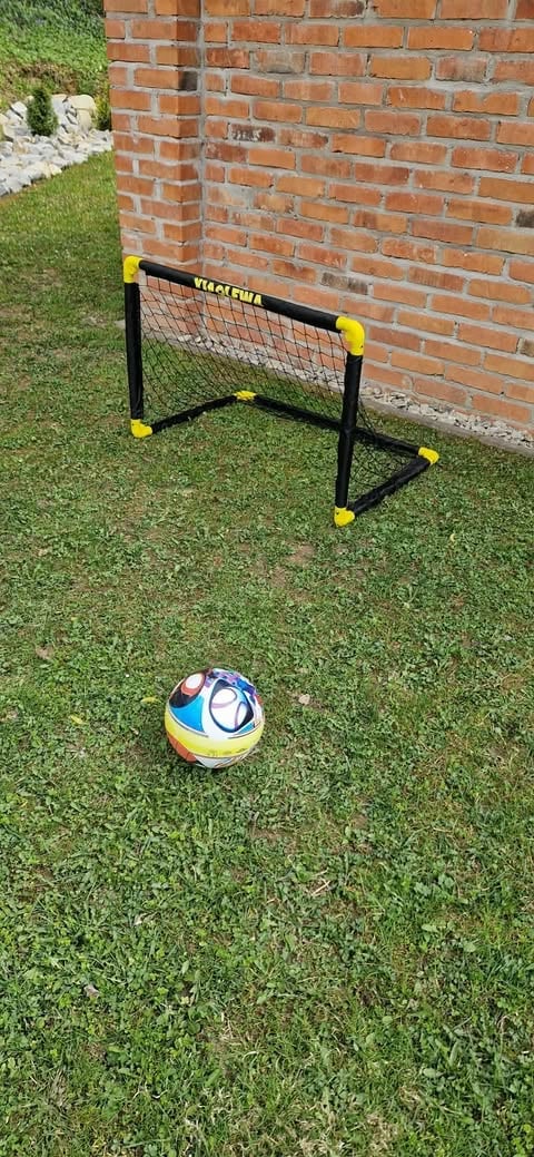 Portable soccer goal with yellow and black frame on grass with a colorful soccer ball in front, red brick wall background