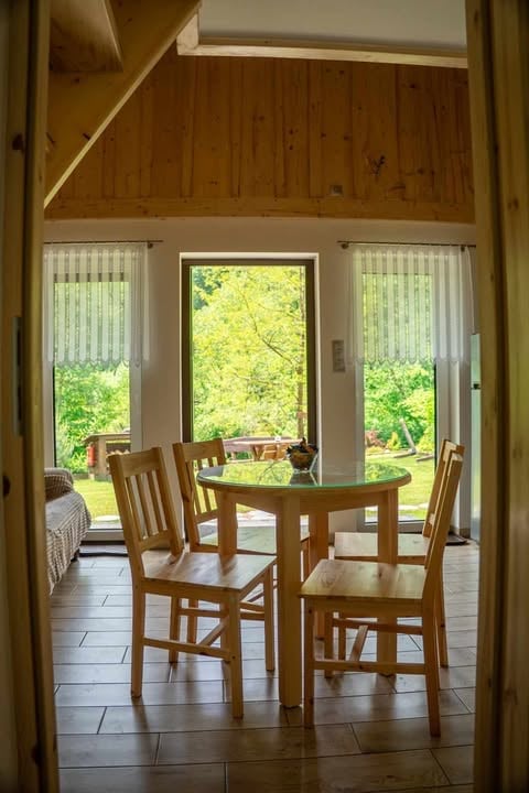 Wooden dining table with chairs in a bright room with glass doors overlooking green trees and garden