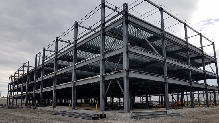 Multi-story steel frame building under construction with exposed structural framework and columns against a cloudy sky