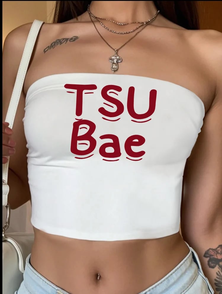 Person wearing a white crop top with TSU Bae text in maroon, layered necklaces, and tattoos visible on shoulder and ribs