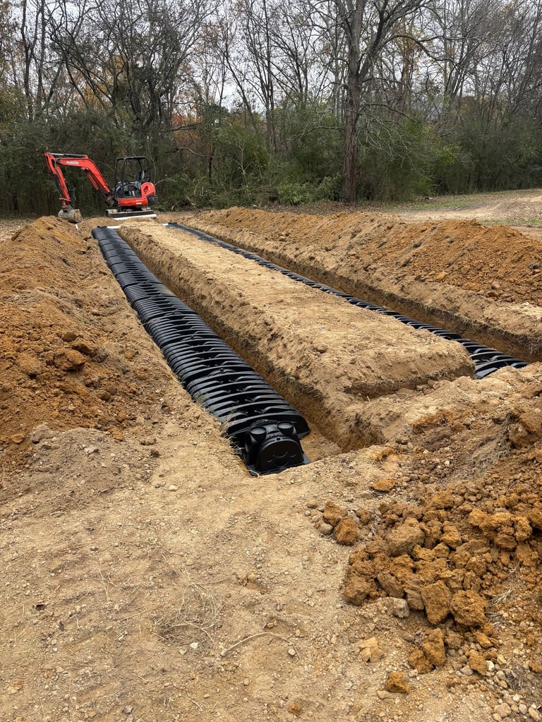Red mini excavator digging a trench and laying black corrugated drain pipes