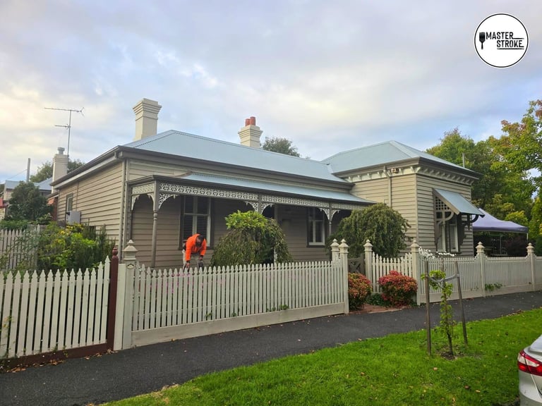 Victorian cottage with white picket fence, green metal roof, and manicured garden, fronted by driveway and lawn