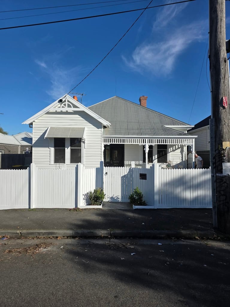 White weatherboard house with pitched roof, front porch, and white picket fence under clear blue sky