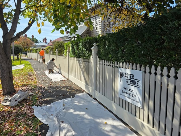 White picket fence along residential street with fall foliage and mature trees, Master Stroke sign visible on fence