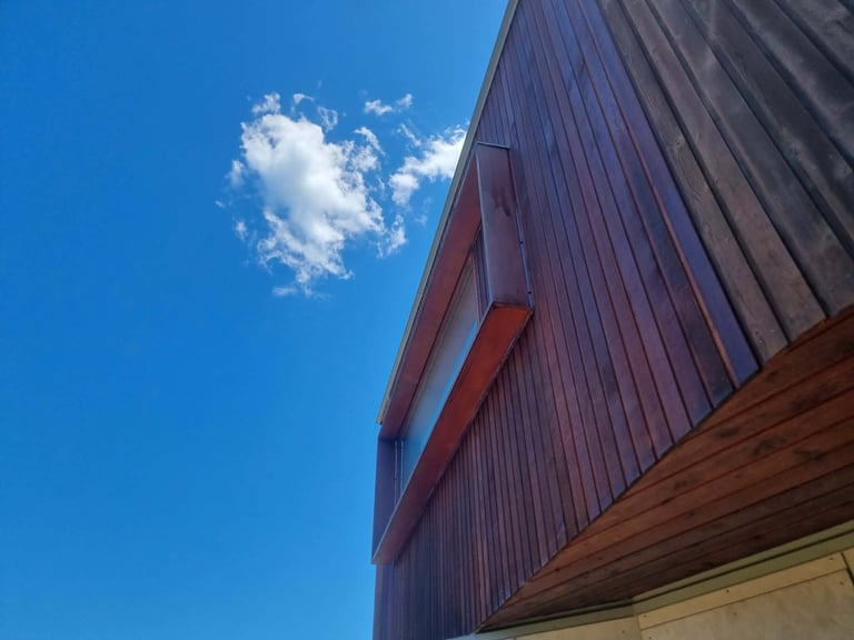 Modern building with burgundy corrugated metal siding and geometric red beam accents against blue sky with white cloud