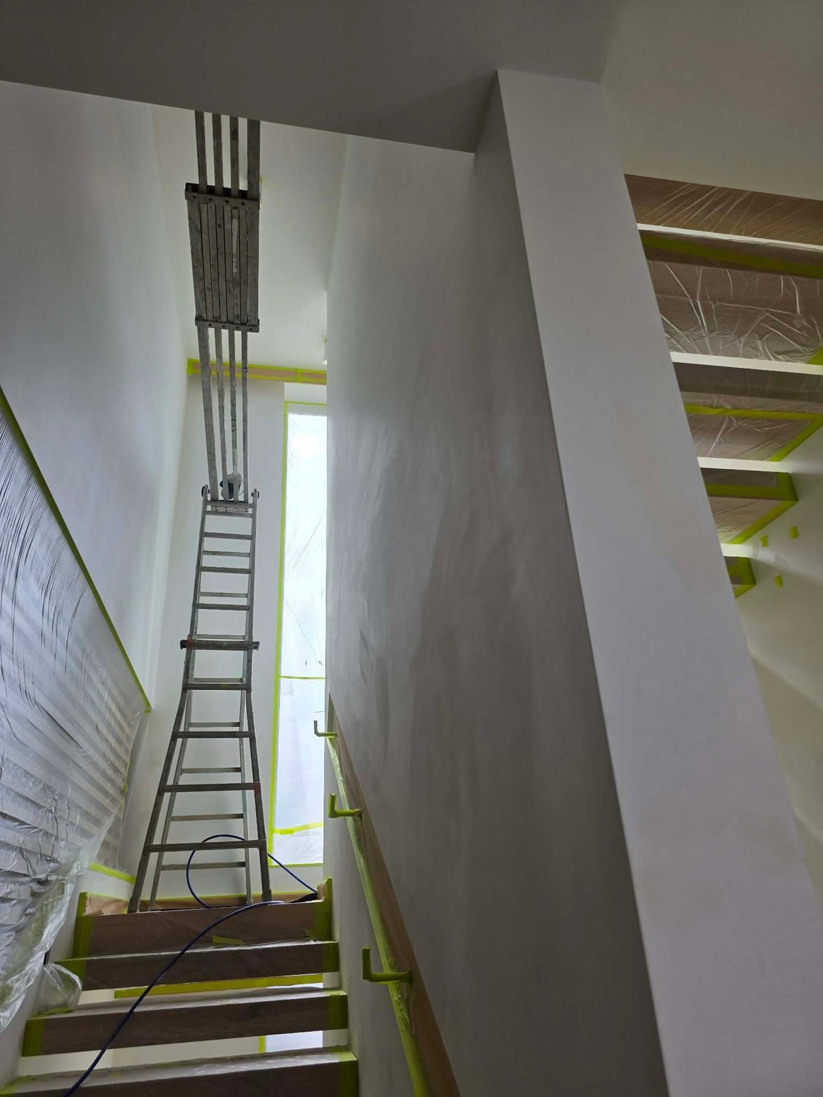 Tall metal ladder leaning against white walls in a narrow interior construction space with yellow safety markings.