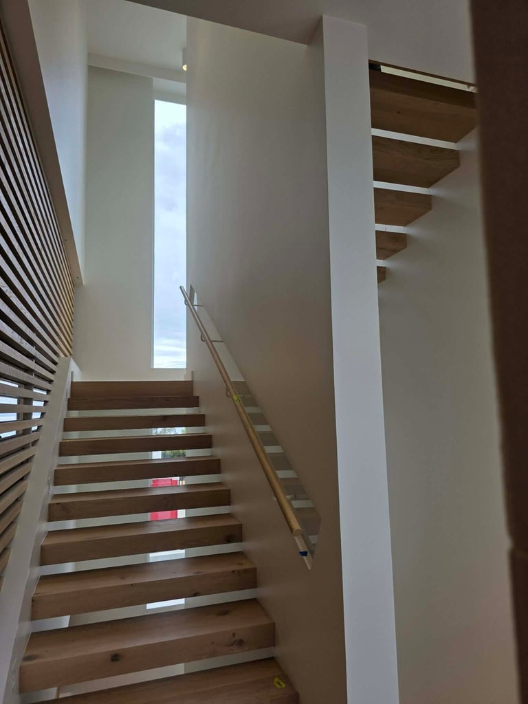 Modern staircase with wooden steps and metal handrail ascending between white walls with natural light from above