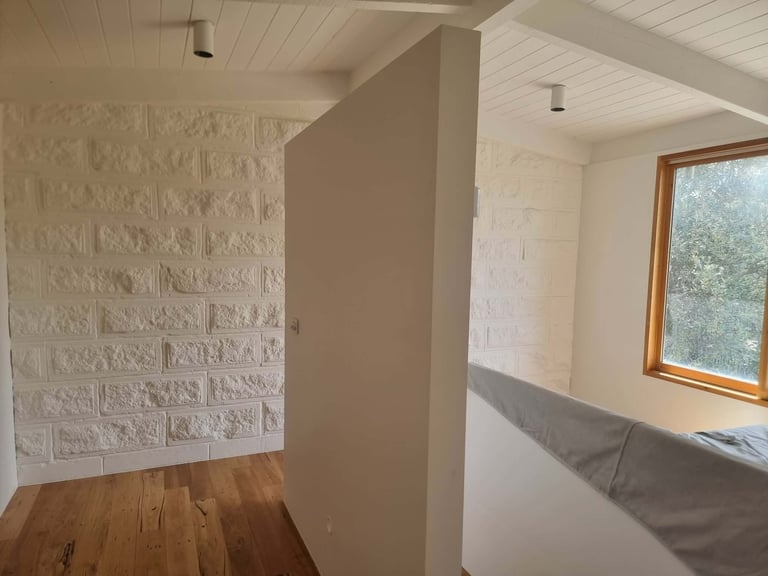 Interior room with white brick wall, tan partition wall, wooden floor, white ceiling, and window with wooden frame