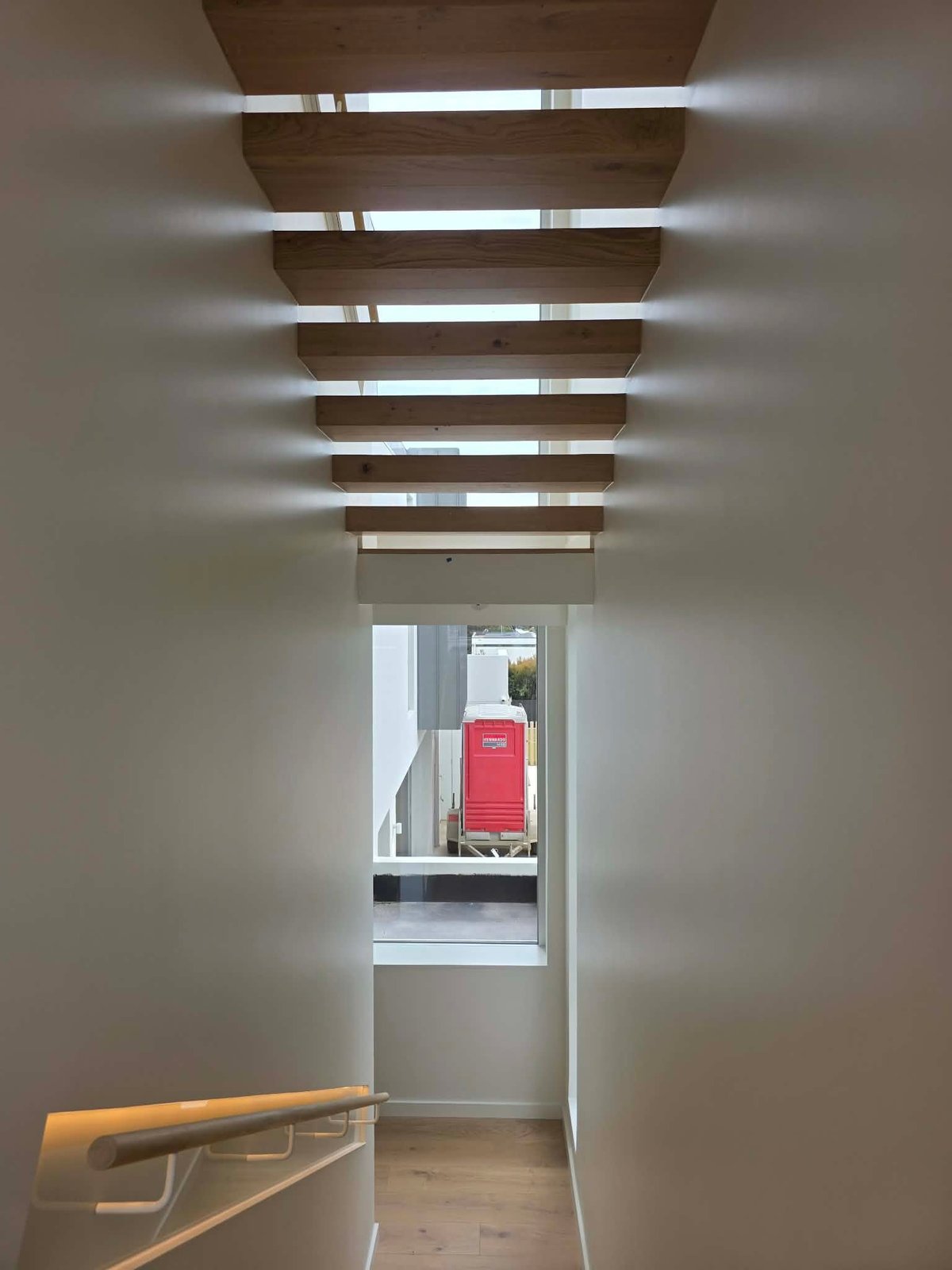 Modern hallway with exposed wooden beams and recessed lighting leading to an exterior door with red accent visible outside