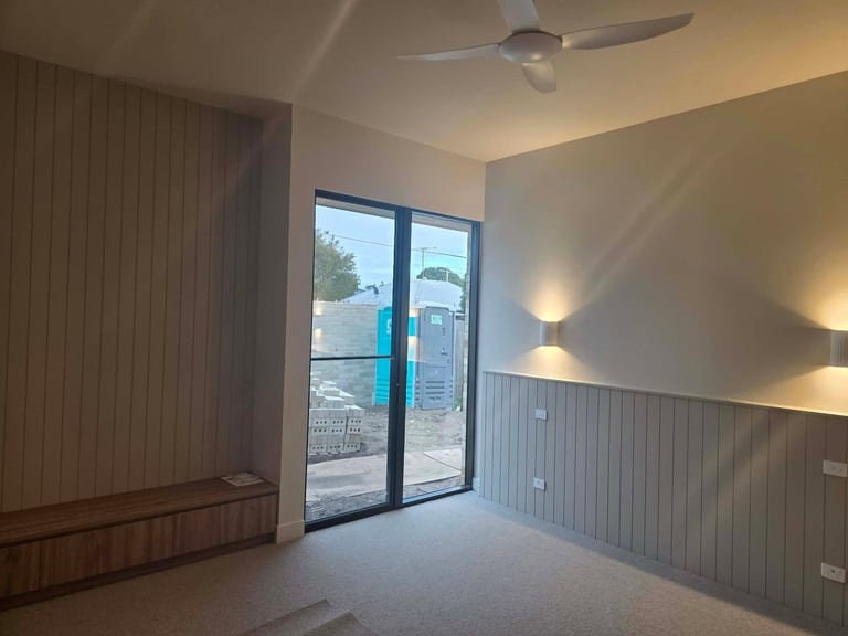 Empty room with sliding glass doors, ceiling fan, wooden wall paneling, and ambient wall lighting