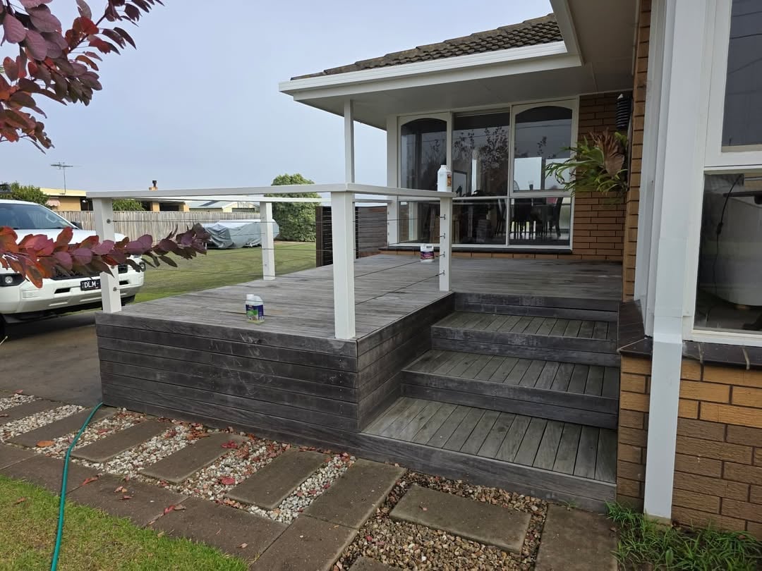 Modern house with gray composite deck, white railings, and covered porch area with brick foundation and landscaping