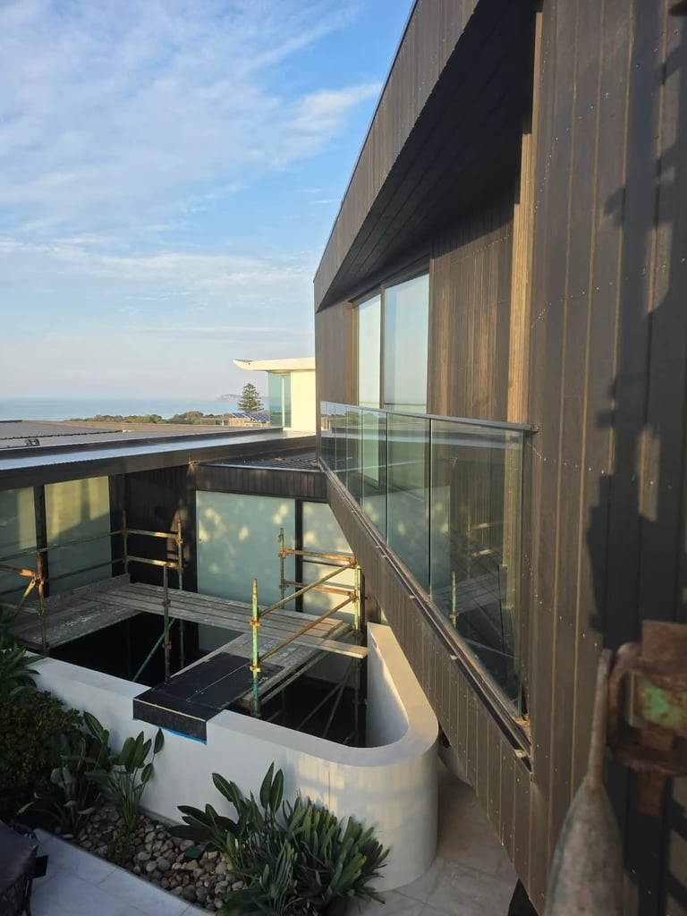 Modern waterfront building with wooden cladding, glass railings, and a sunken seating area overlooking a calm water landscape