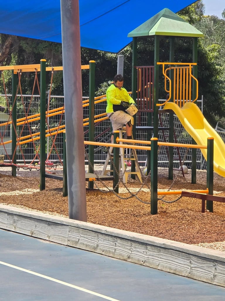 Child in yellow jacket playing on playground equipment with yellow slide and climbing structures under clear blue sky