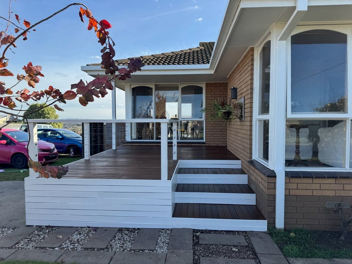 Modern brick house with white trim and deck featuring steps, parked cars visible, autumn foliage in foreground